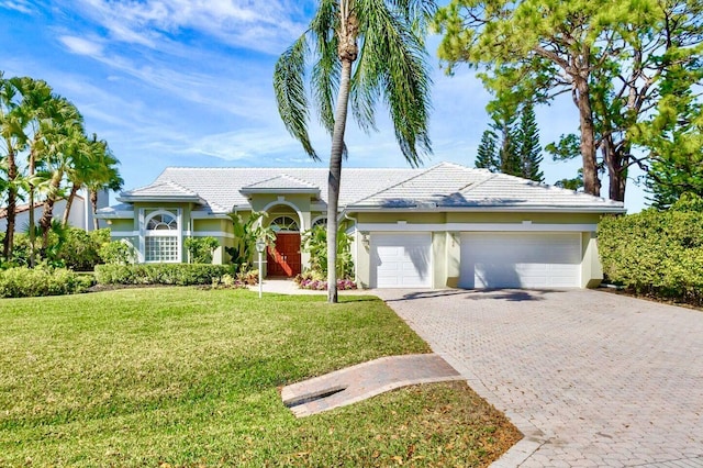 view of front facade featuring stucco siding, a front lawn, decorative driveway, an attached garage, and a tiled roof