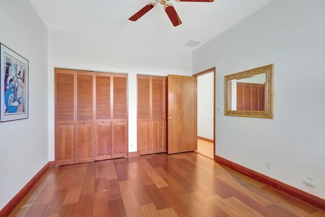 unfurnished bedroom featuring ceiling fan, two closets, and light wood-type flooring