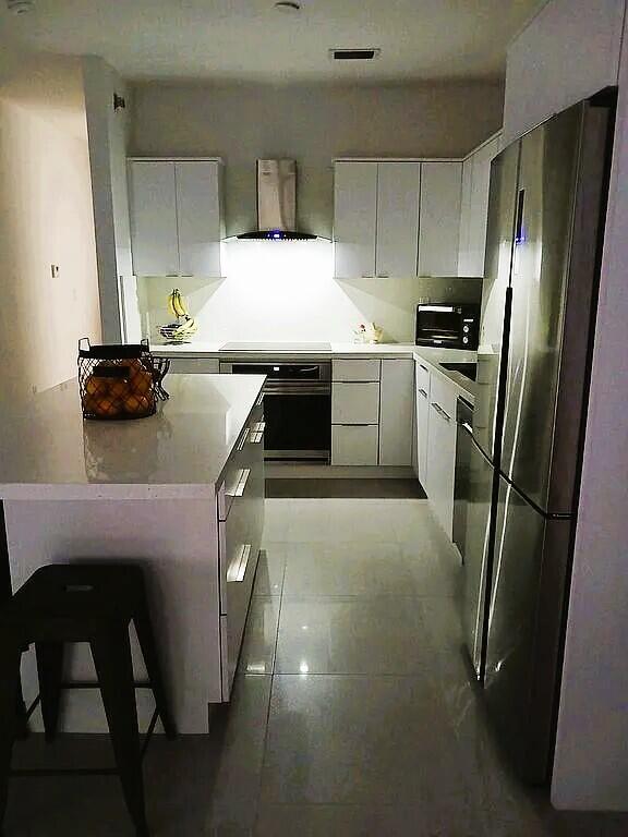 kitchen with stainless steel refrigerator, ventilation hood, stovetop, oven, and white cabinets