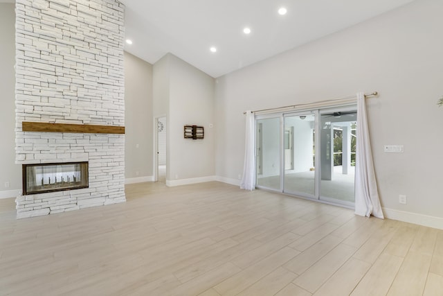 unfurnished living room featuring a towering ceiling, light wood-type flooring, and a stone fireplace