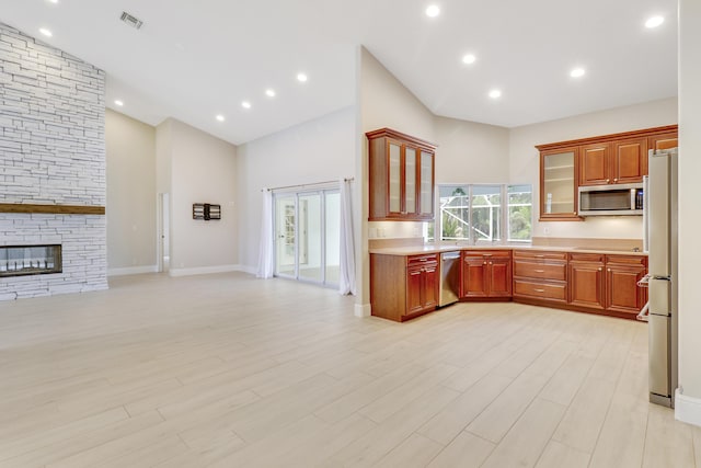 kitchen featuring a stone fireplace, light hardwood / wood-style flooring, high vaulted ceiling, and stainless steel appliances