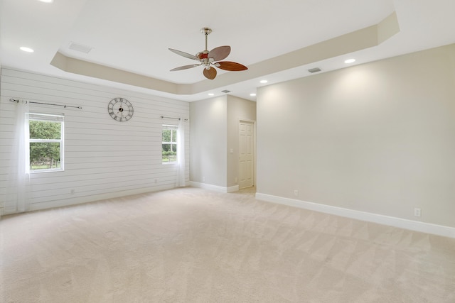 empty room featuring ceiling fan, light colored carpet, and a tray ceiling