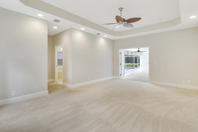 empty room with light colored carpet, a raised ceiling, and ceiling fan