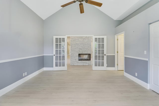 unfurnished living room featuring ceiling fan, a stone fireplace, light hardwood / wood-style flooring, and french doors