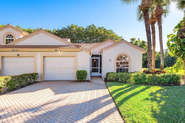 mediterranean / spanish-style house with an attached garage, a front lawn, decorative driveway, and stucco siding