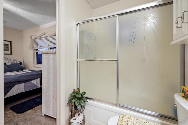 ensuite bathroom featuring connected bathroom, toilet, bath / shower combo with glass door, and a textured ceiling