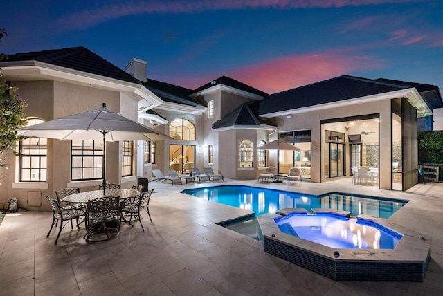 pool at dusk with an in ground hot tub and a patio area