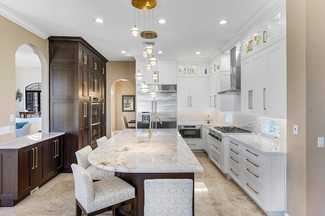 kitchen with appliances with stainless steel finishes, backsplash, wall chimney exhaust hood, a kitchen island with sink, and decorative light fixtures