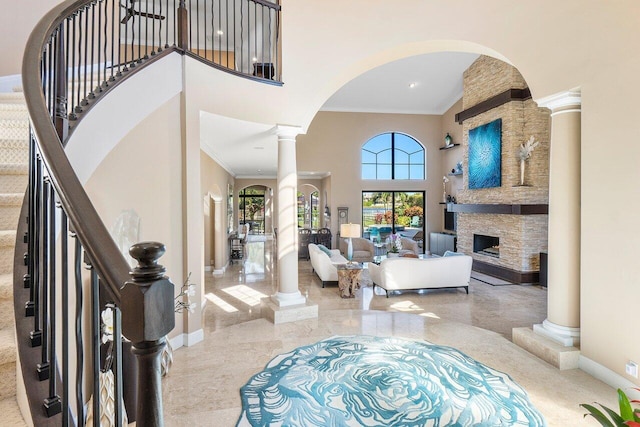 foyer entrance with a stone fireplace, crown molding, a high ceiling, and decorative columns