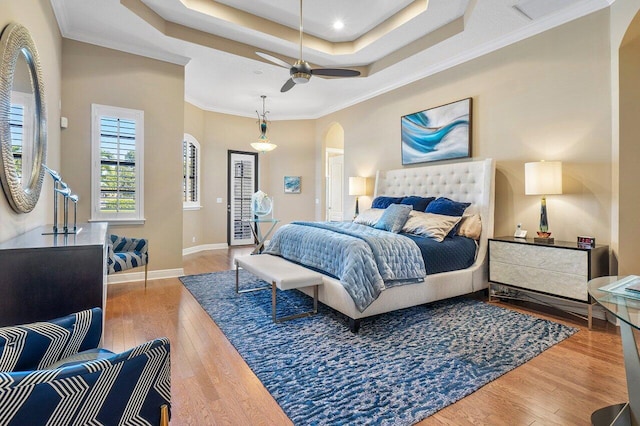 bedroom with hardwood / wood-style flooring, a raised ceiling, ceiling fan, and crown molding