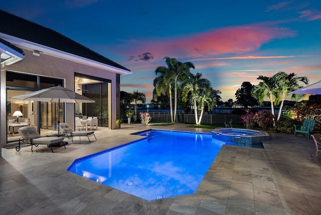 pool at dusk with an in ground hot tub and a patio