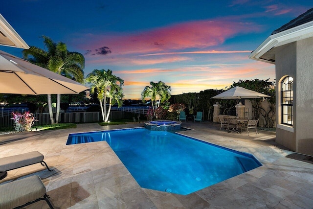 pool at dusk with an in ground hot tub and a patio area