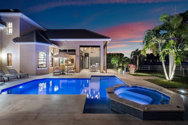 pool at dusk with an in ground hot tub, outdoor lounge area, and a patio area