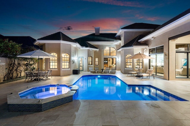 pool at dusk featuring an in ground hot tub, french doors, and a patio