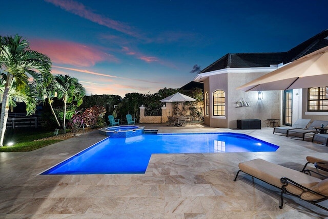 pool at dusk with an in ground hot tub and a patio