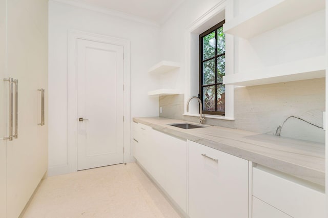 kitchen with sink, white cabinetry, light stone counters, ornamental molding, and backsplash