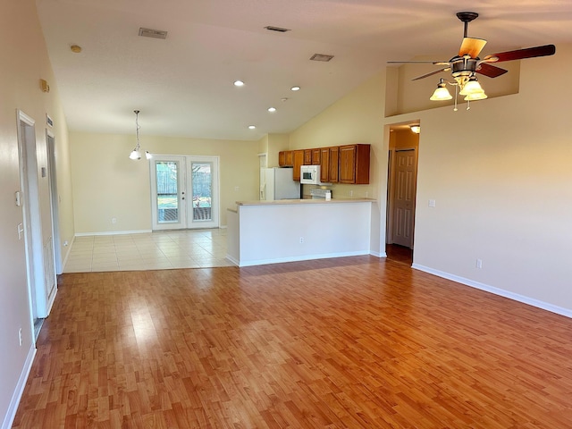 unfurnished living room with french doors, high vaulted ceiling, ceiling fan with notable chandelier, and light wood-type flooring