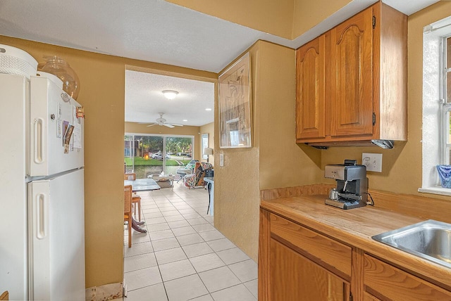 kitchen featuring ceiling fan, sink, white fridge, a textured ceiling, and light tile patterned flooring