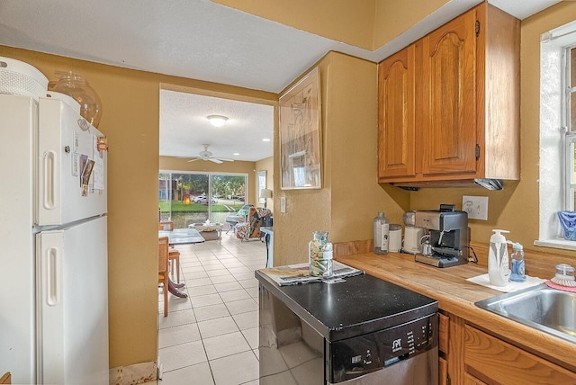 kitchen featuring white refrigerator, sink, ceiling fan, light tile patterned floors, and a textured ceiling