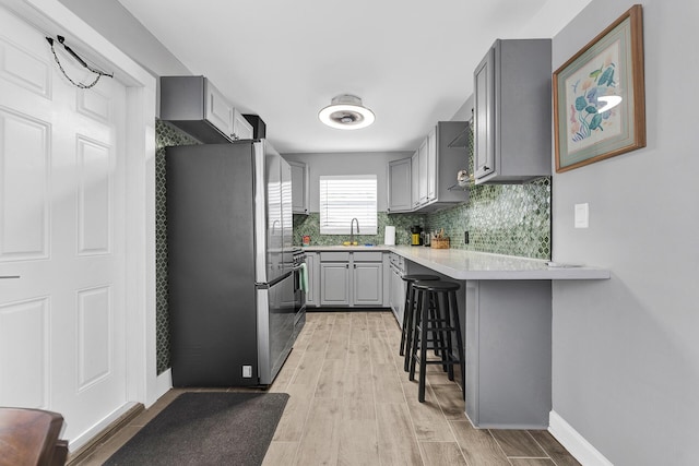 kitchen featuring a kitchen breakfast bar, kitchen peninsula, stainless steel fridge, gray cabinets, and light wood-type flooring