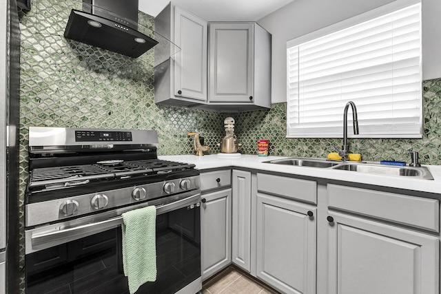 kitchen featuring wall chimney range hood, sink, gray cabinets, light tile patterned floors, and stainless steel range with gas stovetop