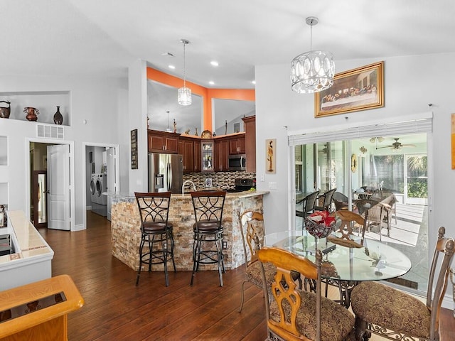 dining room with ceiling fan with notable chandelier, washer / dryer, lofted ceiling, and dark wood-type flooring