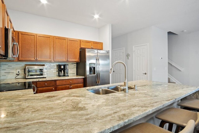 kitchen with appliances with stainless steel finishes, tasteful backsplash, light stone counters, sink, and a breakfast bar area