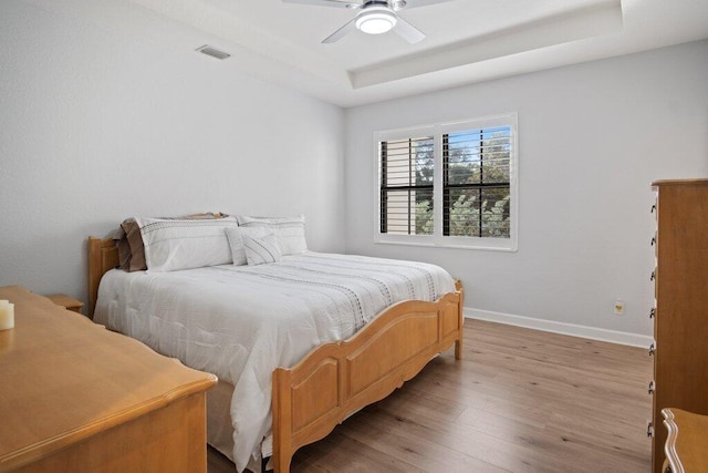 bedroom with a raised ceiling, ceiling fan, and light hardwood / wood-style flooring