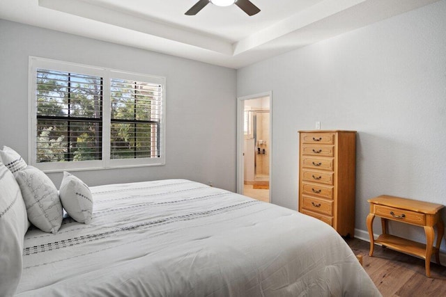 bedroom with hardwood / wood-style floors, connected bathroom, a tray ceiling, and ceiling fan