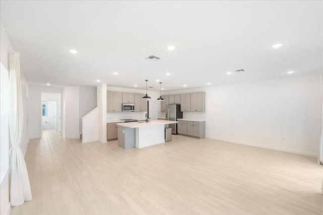 kitchen with gray cabinetry, stainless steel appliances, pendant lighting, a kitchen island with sink, and light wood-type flooring