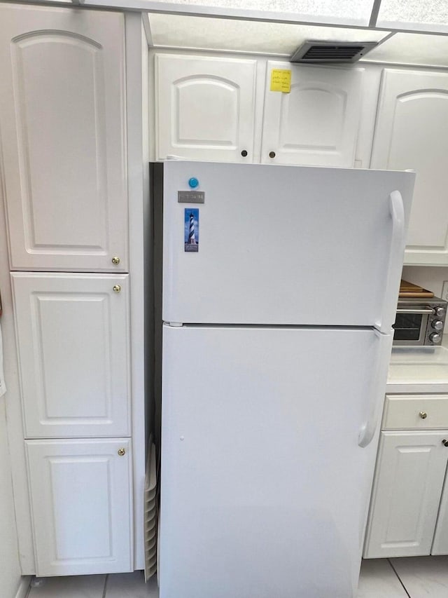 kitchen featuring white refrigerator, light tile patterned flooring, and white cabinetry