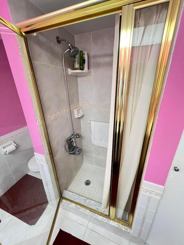 bathroom featuring tile patterned flooring, toilet, walk in shower, and tile walls