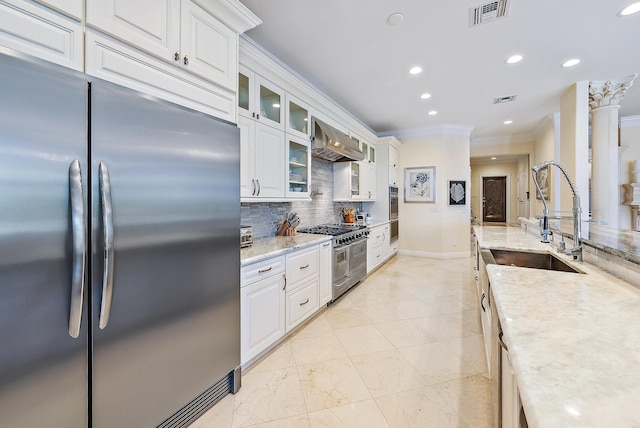 kitchen with wall chimney exhaust hood, high quality appliances, crown molding, and white cabinets