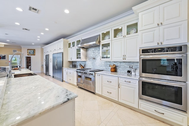 kitchen featuring decorative backsplash, light stone countertops, wall chimney exhaust hood, stainless steel appliances, and white cabinets