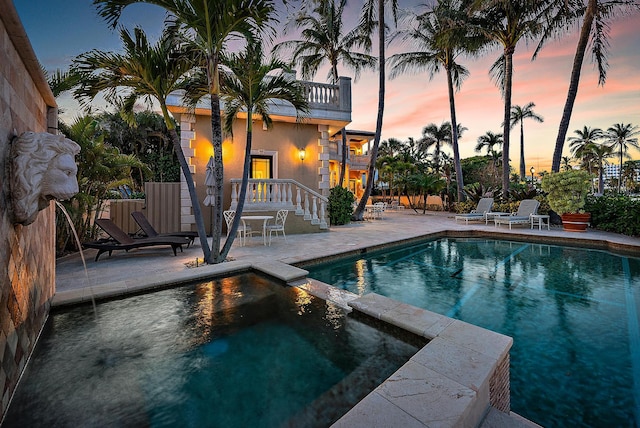 pool at dusk featuring an in ground hot tub and a patio area