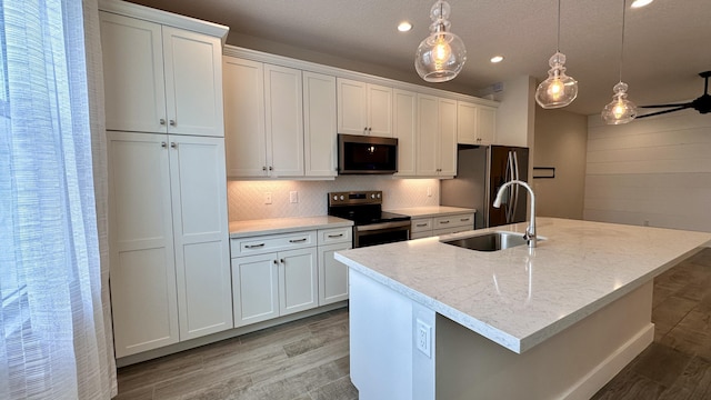 kitchen featuring a kitchen island with sink, sink, white cabinets, and appliances with stainless steel finishes