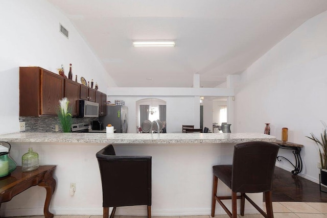 kitchen featuring stainless steel fridge with ice dispenser, backsplash, kitchen peninsula, a breakfast bar area, and light tile patterned floors