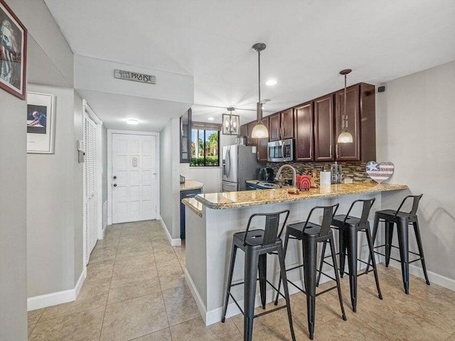 kitchen with kitchen peninsula, pendant lighting, a breakfast bar area, decorative backsplash, and appliances with stainless steel finishes