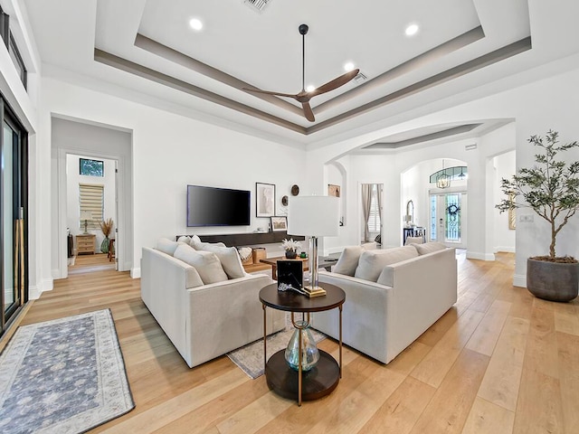 living room with light hardwood / wood-style floors, a tray ceiling, and a notable chandelier