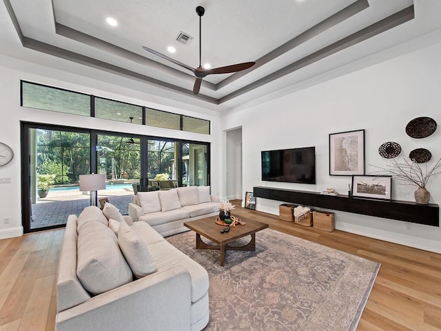 living room featuring a healthy amount of sunlight, a tray ceiling, and light hardwood / wood-style flooring