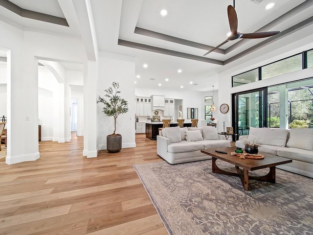 living room featuring ceiling fan, a towering ceiling, a raised ceiling, and light hardwood / wood-style flooring