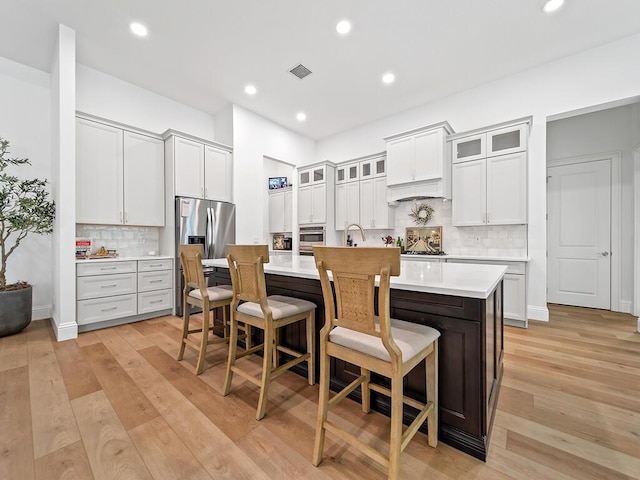 kitchen featuring white cabinetry, a breakfast bar, backsplash, and a center island with sink