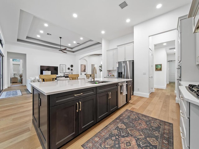 kitchen with appliances with stainless steel finishes, white cabinetry, an island with sink, sink, and ceiling fan