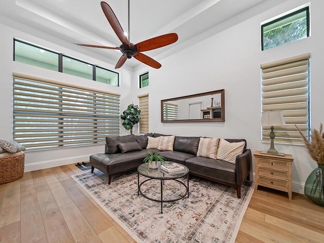 living room with light wood-type flooring, ceiling fan, and a towering ceiling