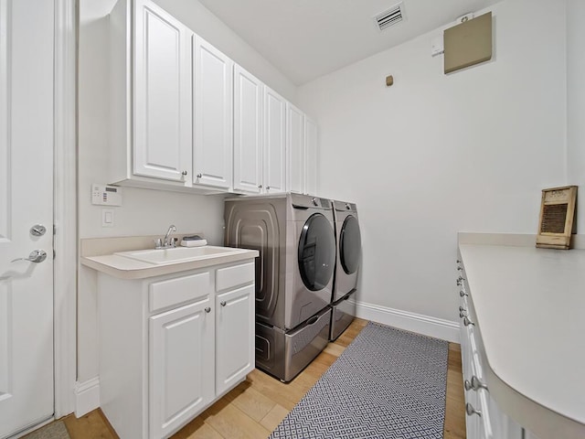 clothes washing area with light hardwood / wood-style flooring, sink, washing machine and clothes dryer, and cabinets