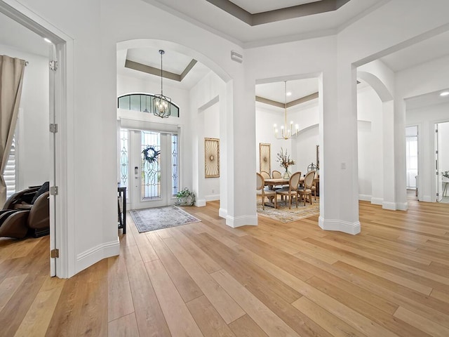 foyer with a high ceiling, a tray ceiling, a chandelier, and light wood-type flooring