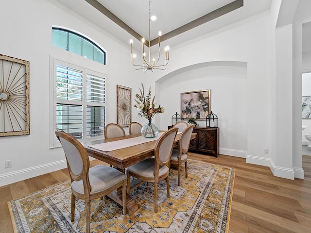 dining area with a chandelier, light hardwood / wood-style flooring, and a raised ceiling