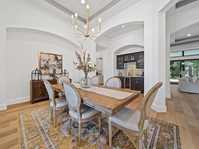 dining space with a raised ceiling, beverage cooler, a chandelier, and light hardwood / wood-style floors