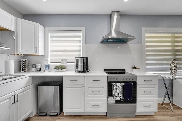 kitchen with wall chimney range hood, light hardwood / wood-style flooring, electric range, fridge, and white cabinetry