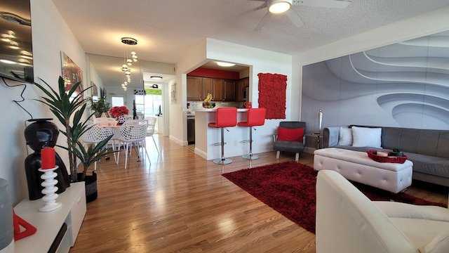 living room with ceiling fan, a textured ceiling, and light wood-type flooring